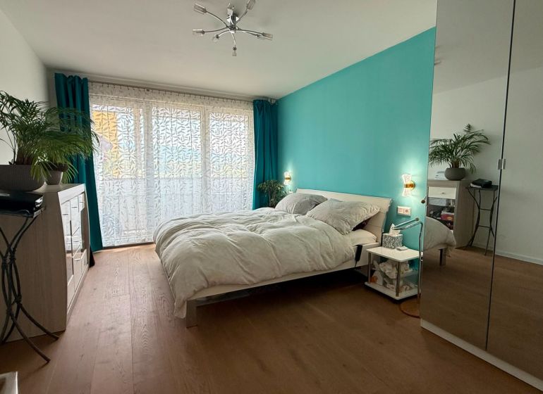 A bright bedroom with a turquoise wall, wood-patterned flooring, and a mirrored wardrobe in a four-room apartment.