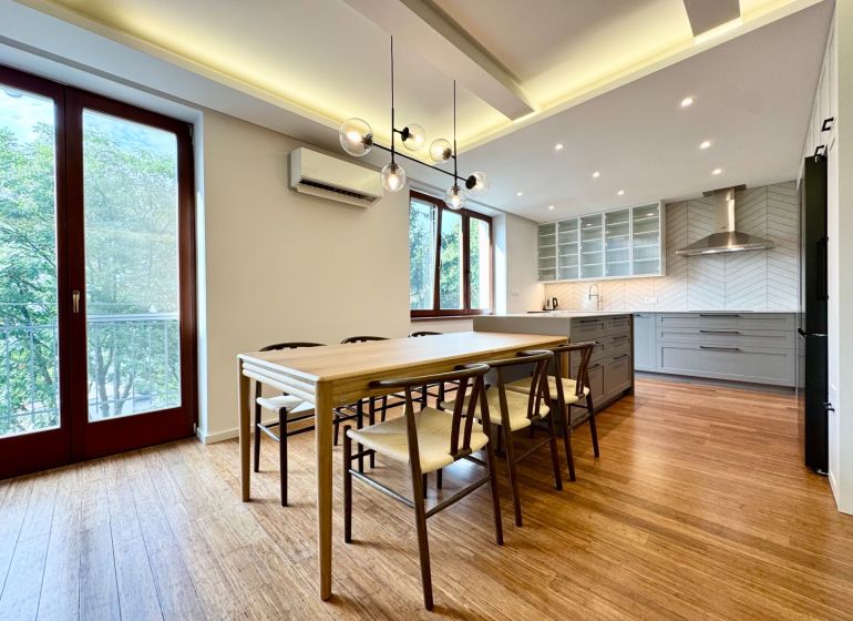 Kitchen in a 3-room apartment, wooden decor flooring, large windows, dining table.