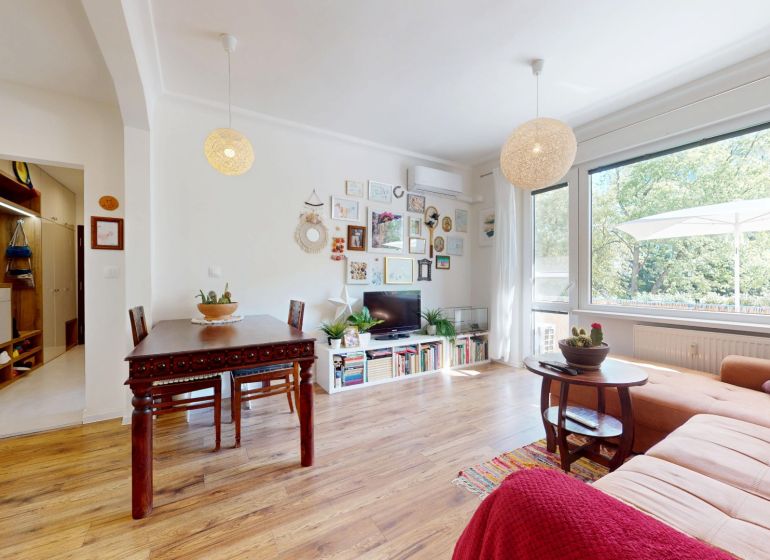 Living room in a 3-room apartment with a wooden decor floor, large window, and decorative elements.