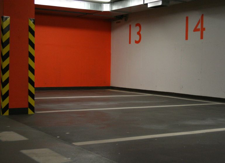 Parking spaces and an orange wall in the garage with yellow and black pillars.