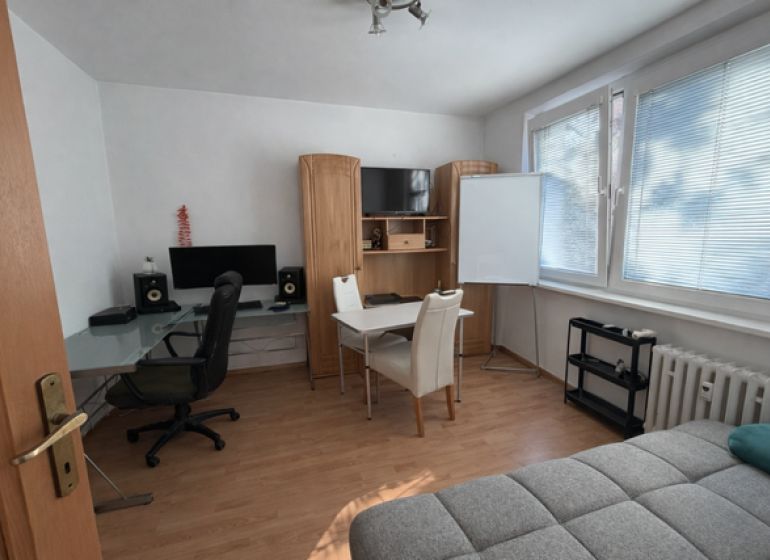 Interior of a 3-room apartment with a wooden decor floor, a desk, and a sofa.