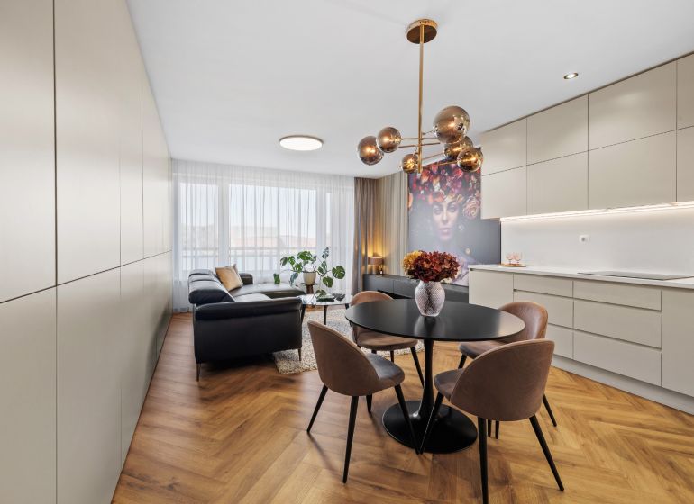 Interior of a 3-room apartment with stylish lighting, a black sofa, decorative art, and a wooden-patterned floor.