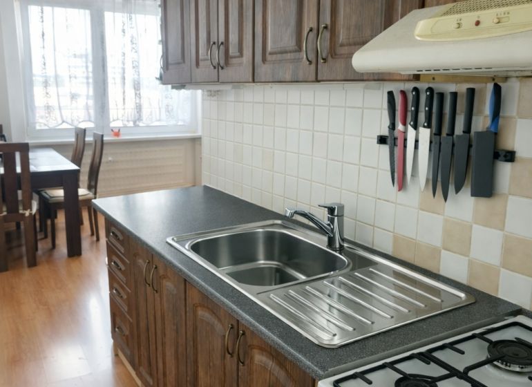 A kitchen in a 3-room apartment with a wooden decor floor and stylish cabinets.