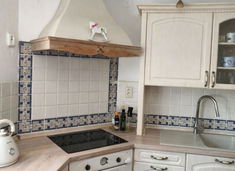 White kitchen with a cooktop, extractor hood, and wooden decor flooring in a family house.