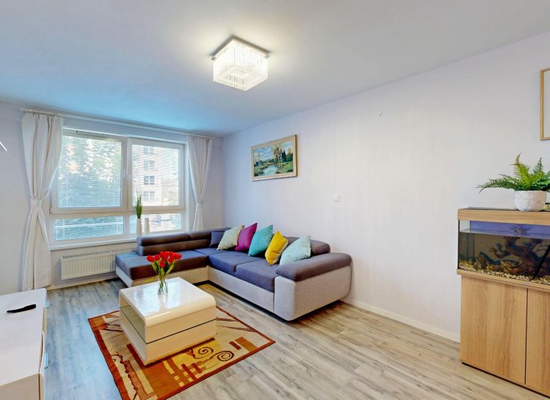Living room in a 3-room apartment with a sofa, an aquarium, a plant, and a floor with a wooden decor.