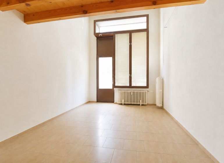 An empty commercial space with a window and a radiator, floor with wooden decor.