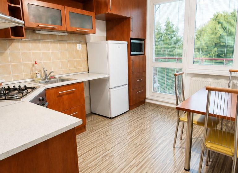 A kitchen in a 2-room apartment with a wooden decor floor and large windows.