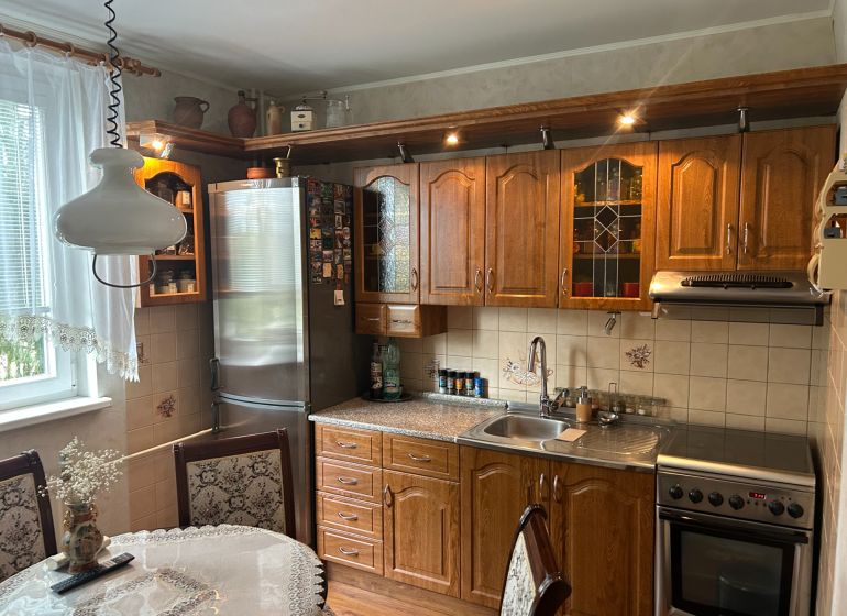 A kitchen in a 3-room apartment with wooden furniture, a decorative curtain, and a dining table.