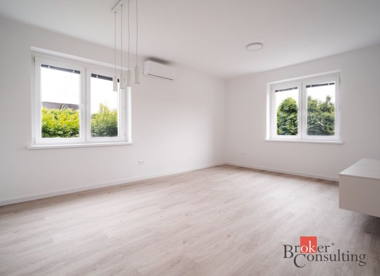 A bright room with wood-patterned flooring and large windows in a three-room apartment.