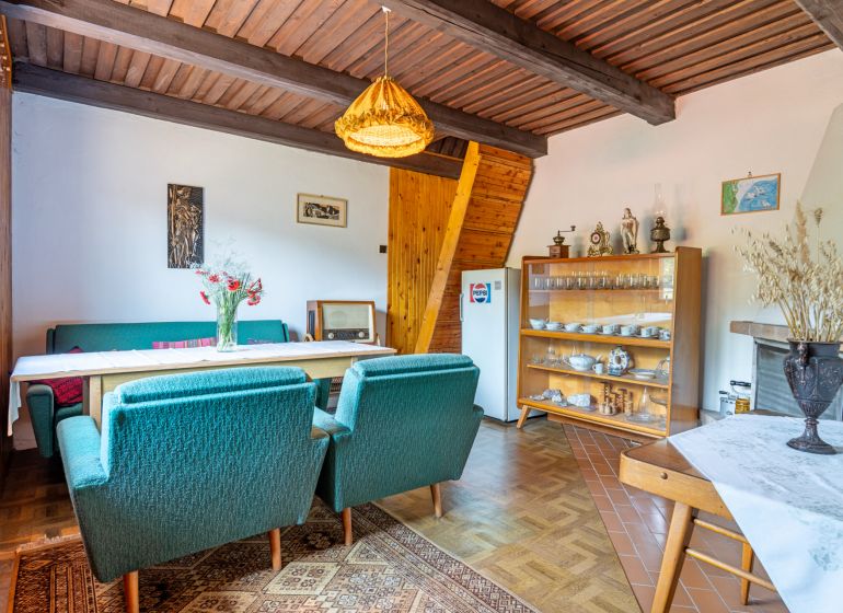 The interior of a cabin with green armchairs, a dining table, and a cabinet with dishes.