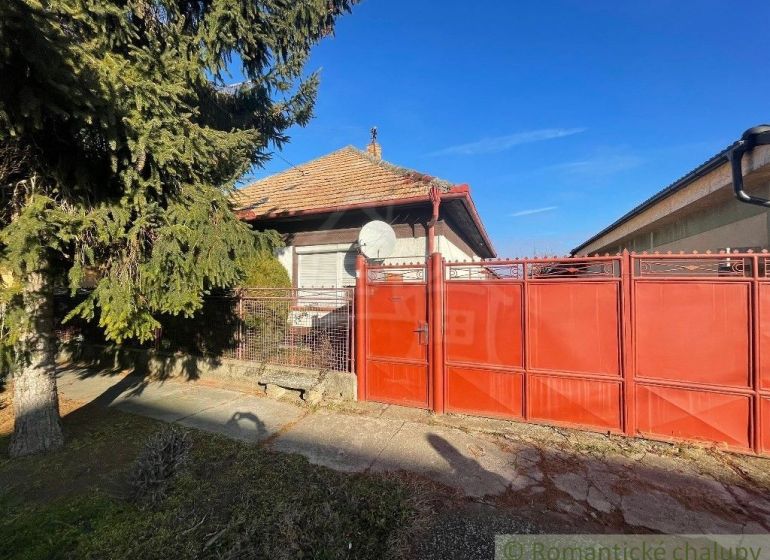 Red gate and fence with a family house in Tvrdošovce, surrounded by greenery.