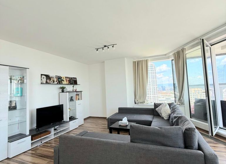 Living room with wood-patterned flooring, a sofa, and a television in a three-room apartment.