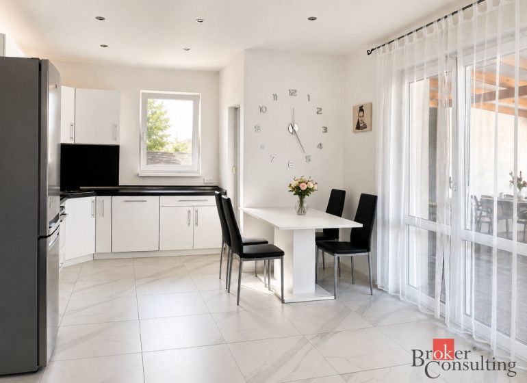 A kitchen in a family house with white furniture and decorative clocks on the wall.