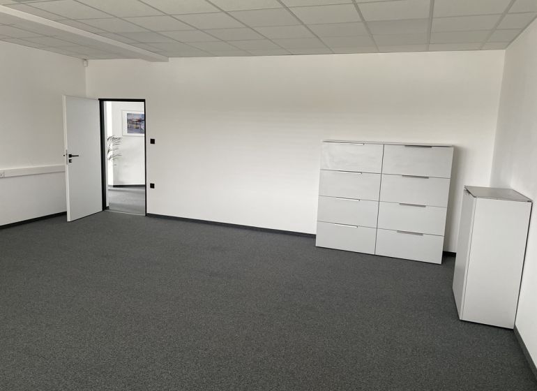 A white office with a dark gray carpet, light furniture, and open doors.