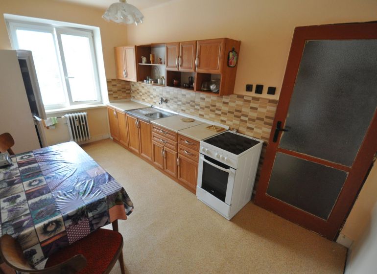 The kitchen of a 2-room apartment with a dining table, kitchen unit, and electric stove.