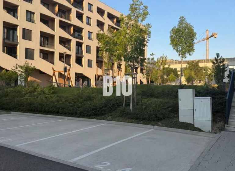 Parking spaces in front of a residential building in Bratislava V, surrounded by greenery and trees.