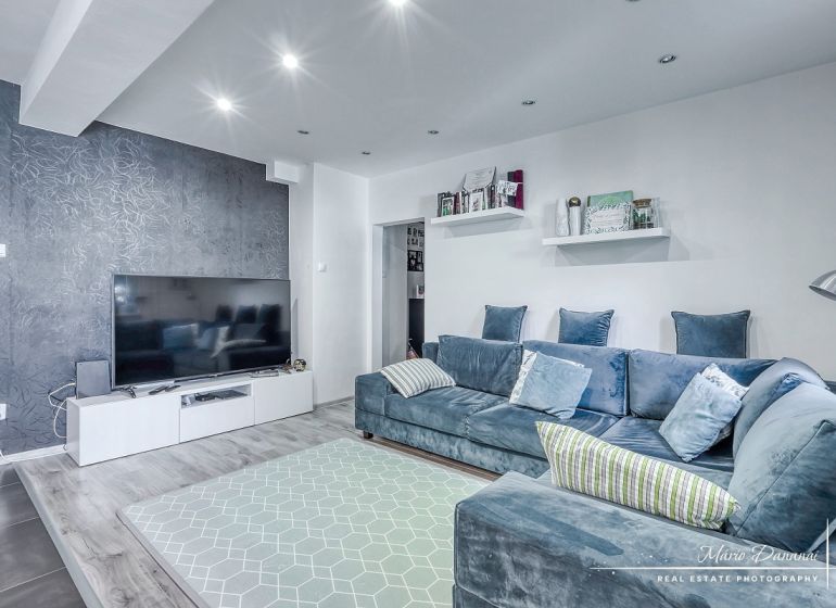 Living room in a 3-room apartment with a large TV, comfortable sofa, and wooden decor flooring.