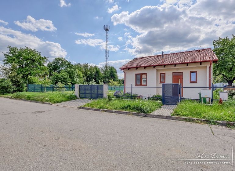 A family house on the street in Kátlovce with an antenna, grass, and a cloudy sky.