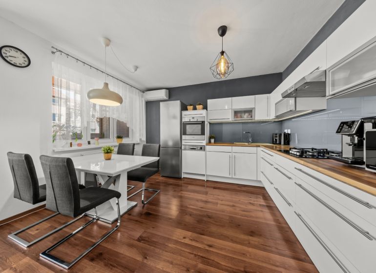 The kitchen of a two-room apartment with white furniture and a floor with a wood decor.