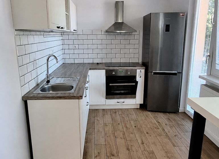 A kitchen in a 2-room apartment with appliances and a wooden decor floor.
