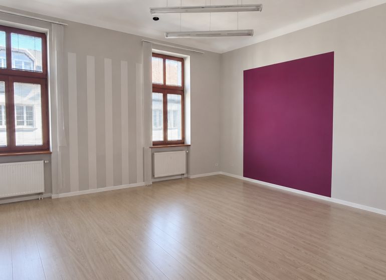 Offices with wood-patterned flooring and a purple wall, large windows, clean lines.