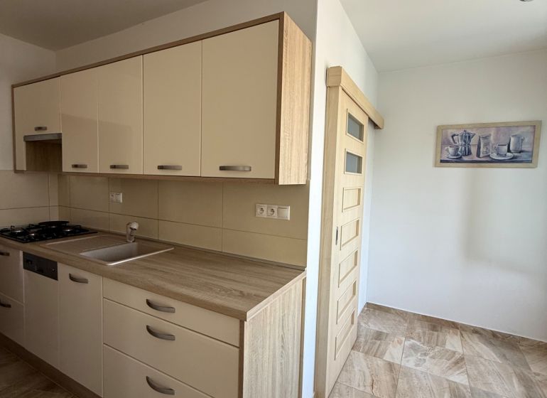 The kitchen of a 3-room apartment with a wooden decor floor and a light-colored kitchen unit.