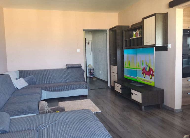 Living room with wood-patterned flooring and a large corner sofa in a 3-room apartment.