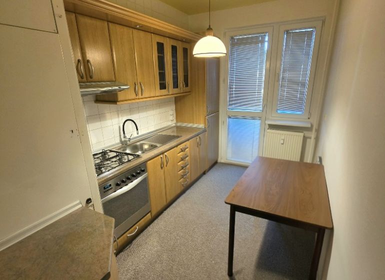A kitchen in a 3-room apartment with wooden furniture, a dining table, and white lighting.