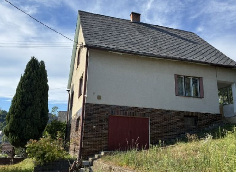 A family house in Lednice with a wooden decor and a sloped roof, surrounded by greenery.