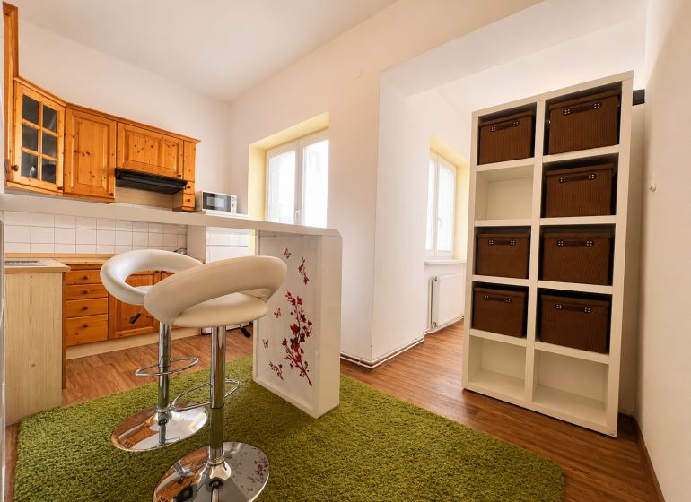 A kitchen in a studio apartment with cabinets, bar stools, and a wood-patterned floor.