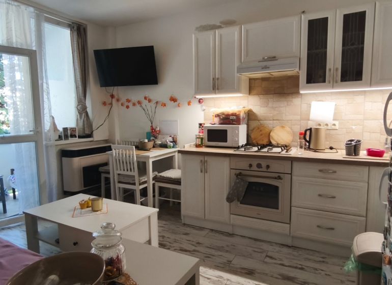 A kitchenette with white cabinets, a dining table, and a wooden decor floor in a studio apartment.