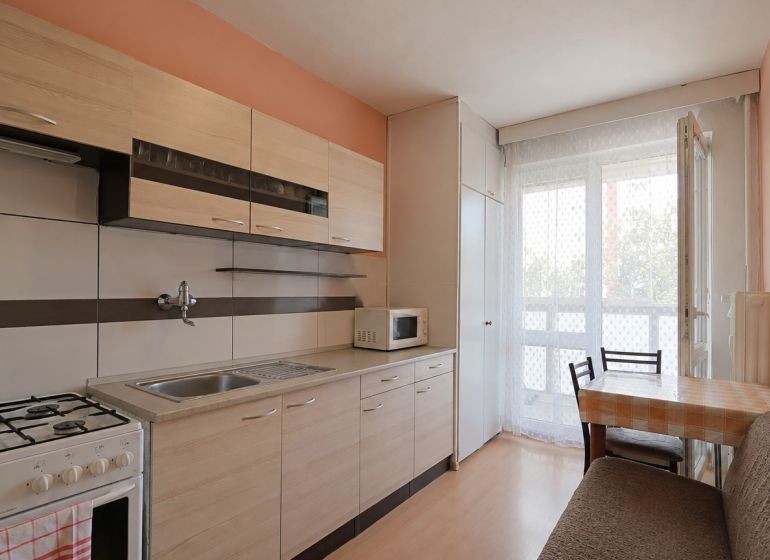 A kitchen in a 3-room apartment with a wooden decor floor and balcony doors.