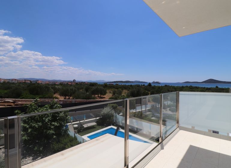 View from the holiday apartment in Tribunj of greenery, pool, and sea.