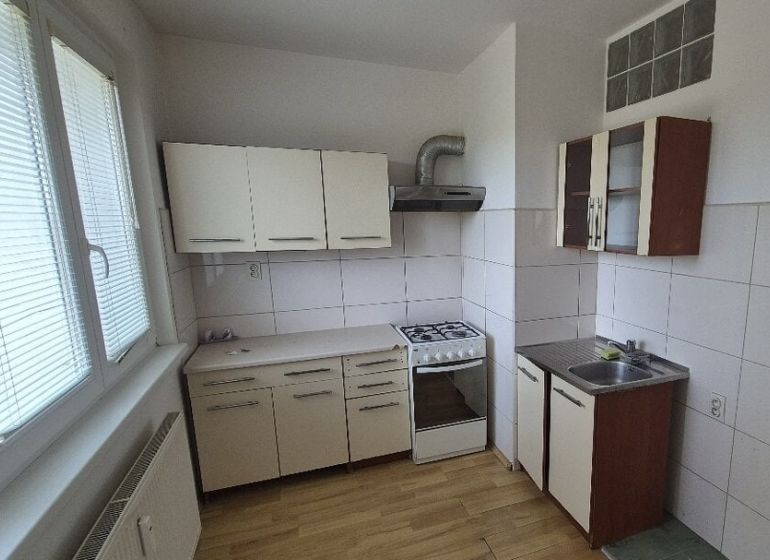 A kitchen in a one-room apartment with a wood-patterned floor and white cabinets.