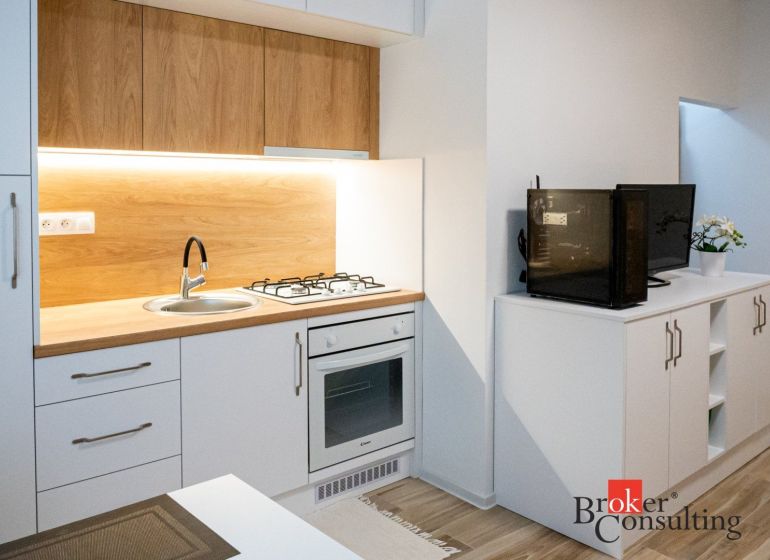 A kitchenette in a studio apartment with a wood decor and appliances.