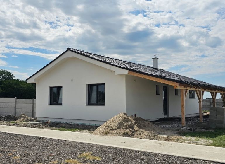 A family house in Bellova Ves with a white facade, a sloped roof, and surrounding buildings.