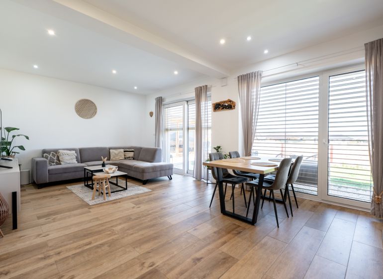 Living room with wood-patterned flooring, large sofa, and dining table in a family house.