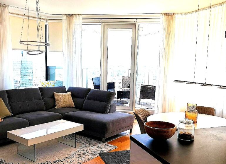 Living room of a three-room apartment with a corner sofa and a table, floor with a wooden decor.