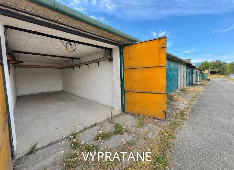 Open garages in Detva with an asphalt access road and blue sky.