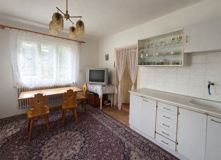 Interior of a family house with a dining area, kitchen unit, television, and table with a wooden decor.