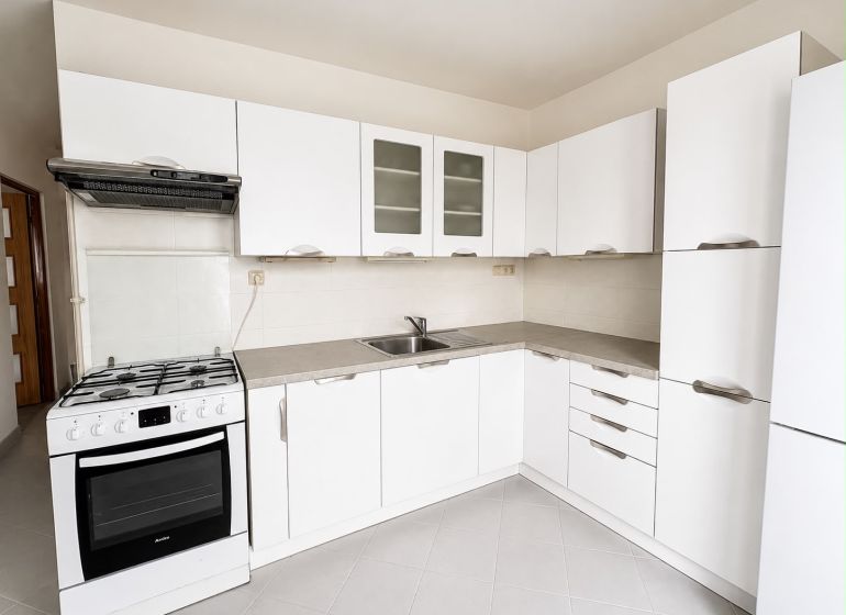 A white kitchen with a gas stove and white cabinets in a two-room apartment.