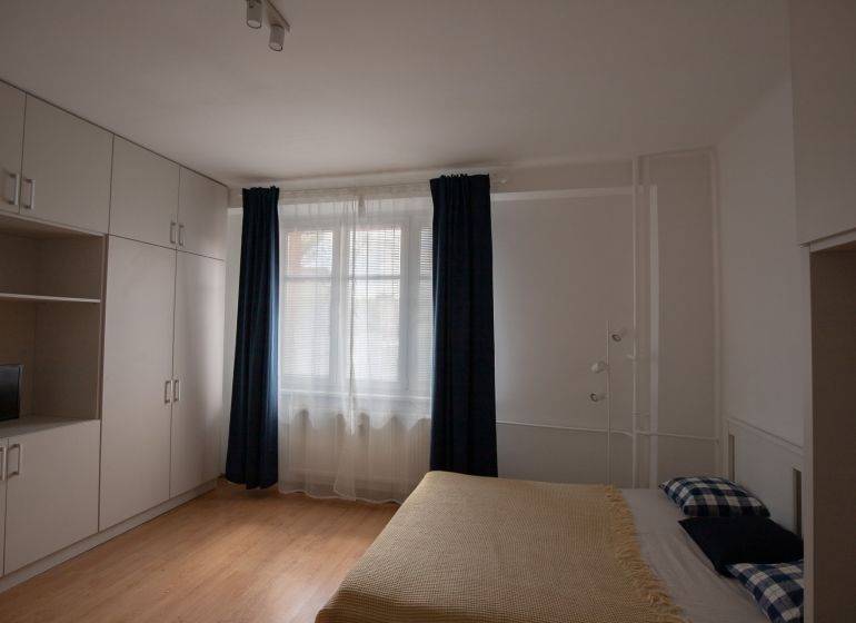 A room in a one-bedroom apartment with a bed, storage spaces, and a floor with a wooden decor.
