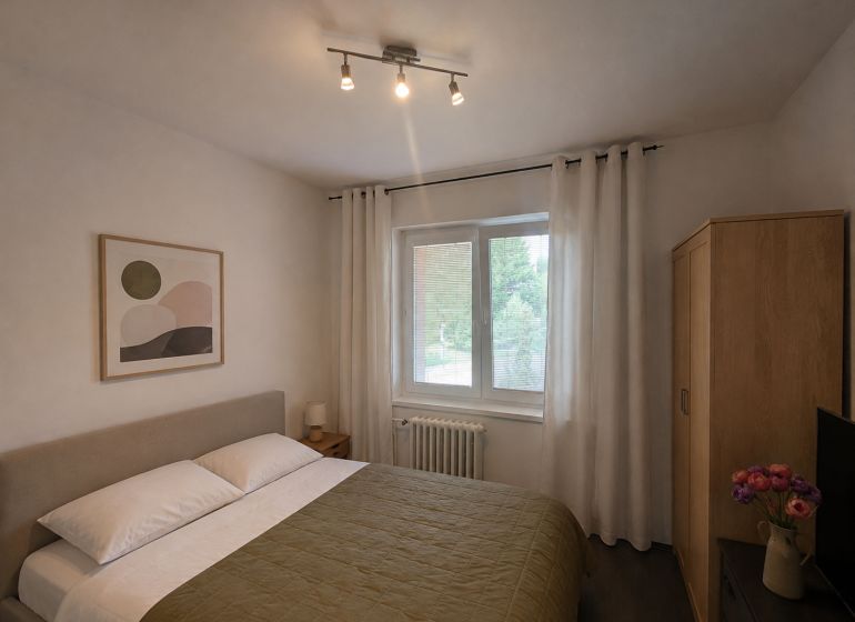 A bedroom in a 4-room apartment with a bed, a painting, and wooden furniture.