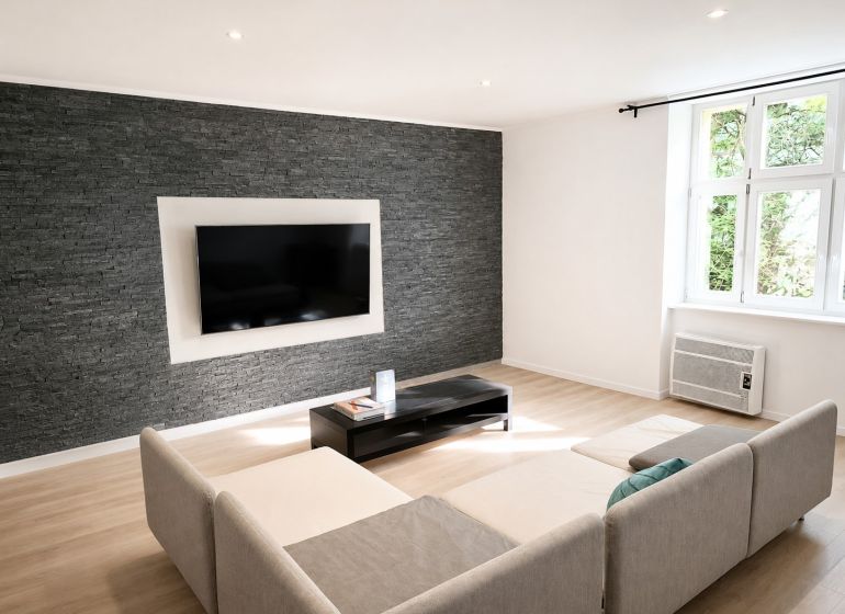 Living room in a 3-room apartment with a gray stone wall and a wooden decor floor.