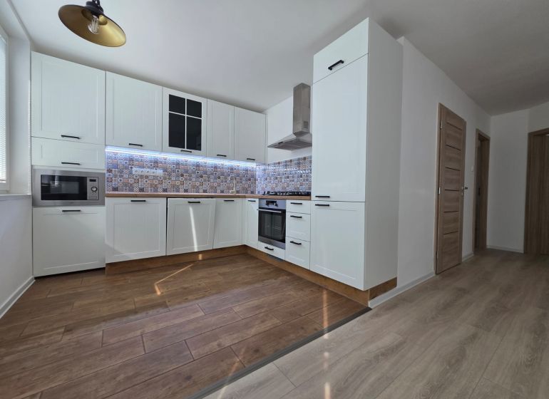 A kitchen in a 3-room apartment with a wood-patterned floor and white cabinets.