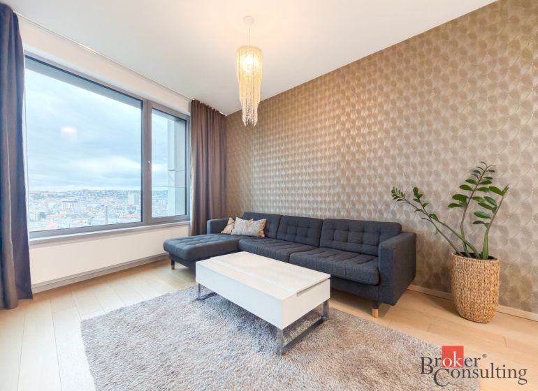 Living room in a 2-room apartment with a sofa, table, plant, and wooden decor flooring.