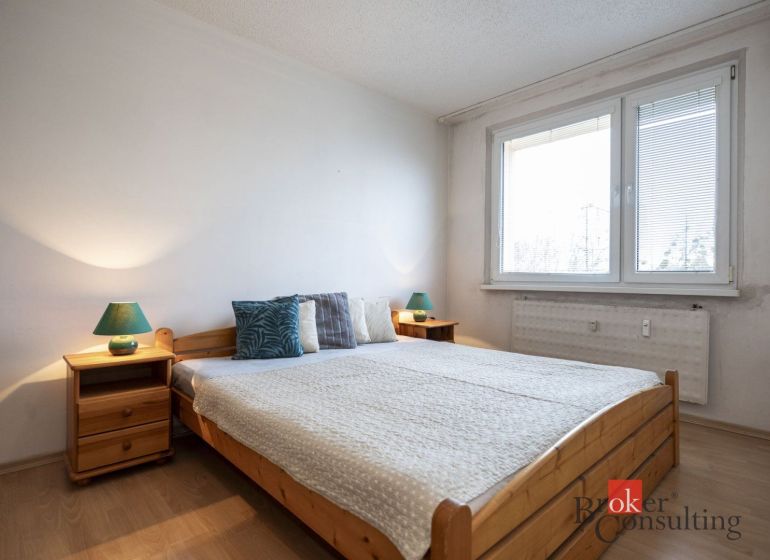 A bedroom with a bed, nightstands, and a wooden decor floor in a 4-room apartment.