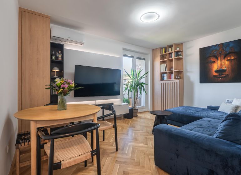 Living room in a 3-room apartment with a wooden decor floor, a comfortable sofa, and a television.