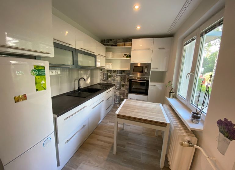 A bright kitchen with white cabinets and a table that has a wood-patterned floor.
