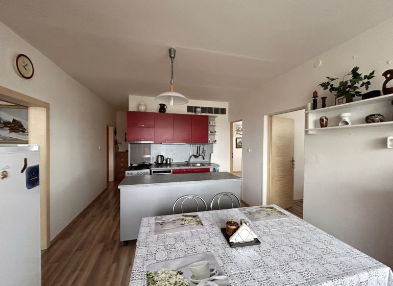 A kitchen in a 3-room apartment with a table, red cabinets, and a floor with a wood decor.